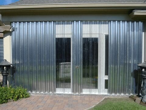 Clear corrugated plastic panels with impact resistance installed on a patio covering large glass doors to protect against weather, providing a transparent barrier while allowing light to pass through. in either North or South Carolina